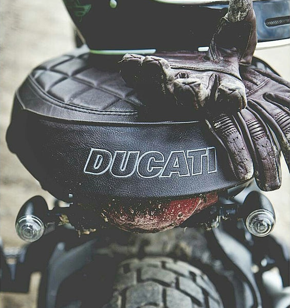 A vintage style motorcycle glove sitting on the seat of a Ducati motorcycle