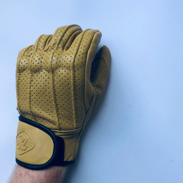 A hand wearing a Speed motorcycle glove by 78 Motor Co., made of yellow perforated leather with knuckle protection and a velcro strap on the wrist with the number '78' embossed on the strap.