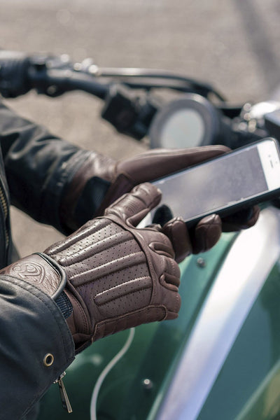 Brown leather motorcycle gloves with a smartphone.